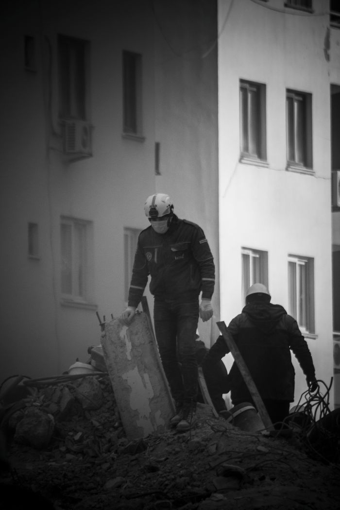 Rescuers navigating rubble in Adana, Turkey following a devastating earthquake. Black and white image captures urgency and resilience.